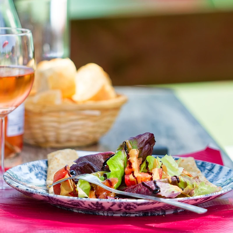 Une salade mélangée présentée dans une assiette à motifs bleus servie avec un verre de rosé