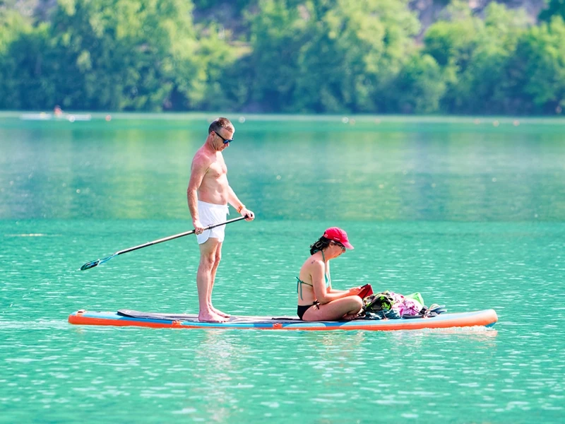 Un home se tient debout sur un paddle et pagaye tandis que sa femme est assise à l'avant et lit un livre.