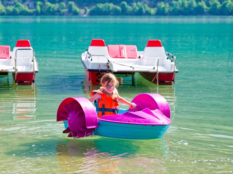 Une petite fille, équipée d'un gilet de sauvetage, fait du mini bateau à pédales sur le lac