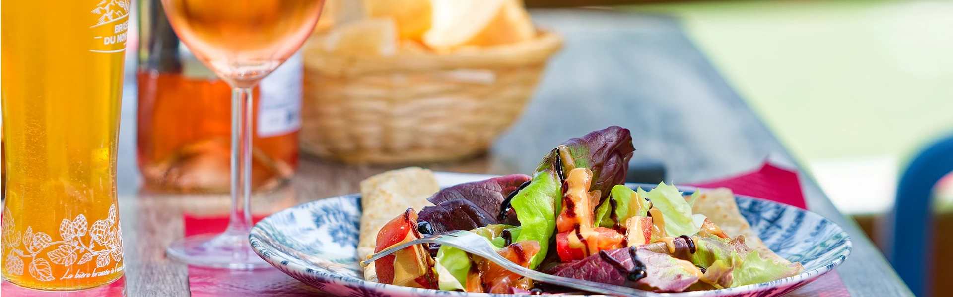 Sur une table de restaurant, on peut voir une appétissante salade mélangée accompagnée d'un verre de rosé