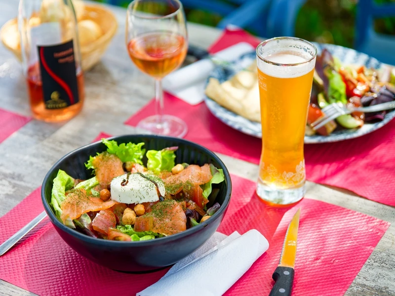 Sur une table de restaurant sont disposées deux assiettes de salades mélangées, un verre de bière et un verre de rosé