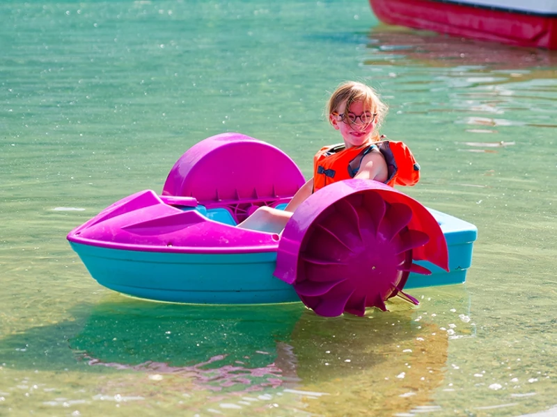 Une petite fille souriante, équipée d'un gilet de sauvetage, fait du mini bateau à pédales.